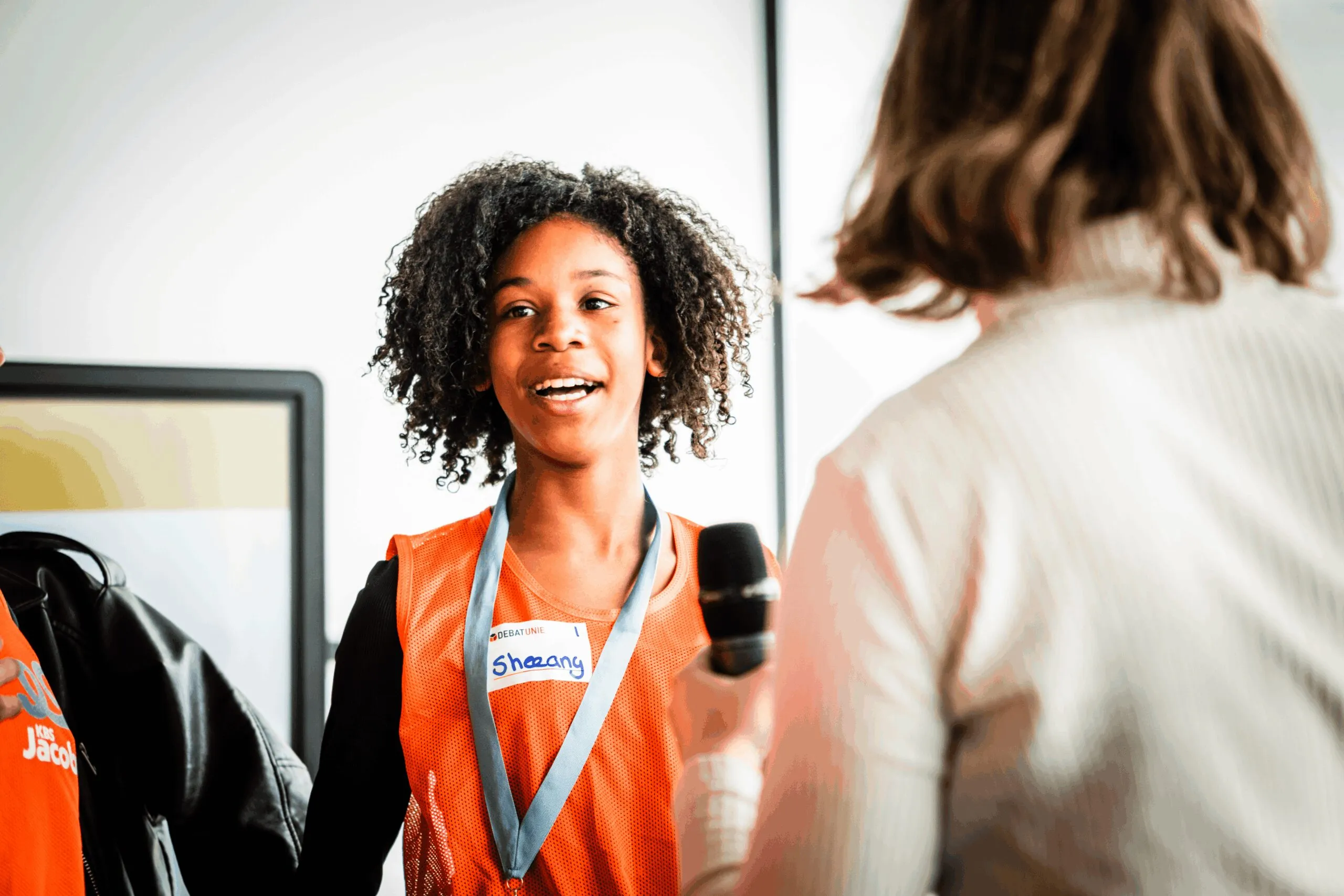 Een lachende leerling spreekt in een microfoon tijdens een debatworkshop
